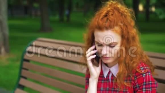 伤心的红头发女孩在公园打电话视频的预览图