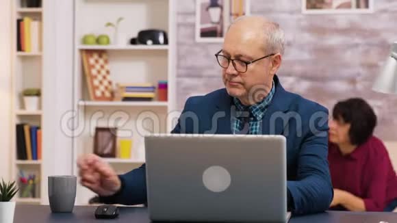 在笔记本电脑上工作的老人一边喝咖啡视频的预览图