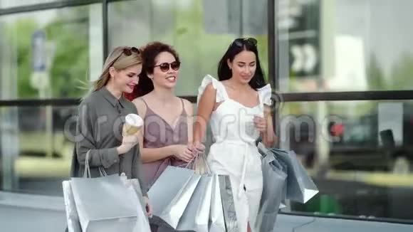 微笑奢侈女性朋友闲谈走路与购买购物袋中平底锅拍摄视频的预览图
