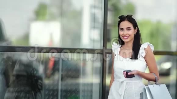 微笑迷人的年轻女人带着购物袋走着看着摄像机视频的预览图