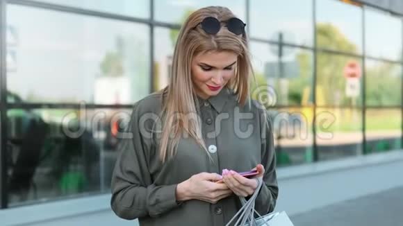 时尚的年轻女性带着购物袋微笑着用智能手机在户外聊天视频的预览图