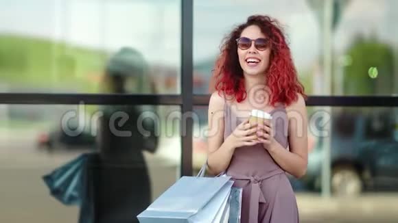 肖像时尚红发女孩带着购物袋享受休息喝咖啡纸杯户外视频的预览图
