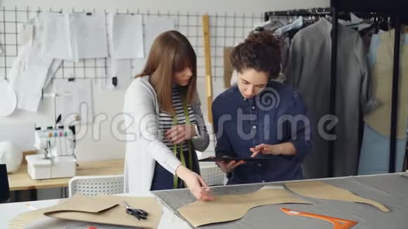 年轻的裁缝正在与平板电脑合作在工作室的办公桌上交流和勾勒出纺织品的服装图案光线视频的预览图