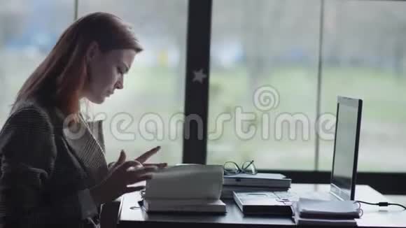 商业上的问题年轻的女企业家坐在靠窗的桌子旁紧张地一边远程工作一边打着笔记本电脑视频的预览图