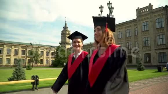两个快乐的女孩在壁炉里走向大学大楼年轻人庆祝他们的毕业典礼视频的预览图