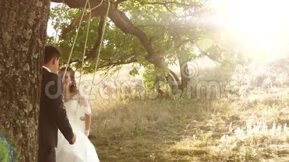 情侣在公园散步快乐的新郎在夏天在摇摆的新娘上摇摆男孩和女孩在橡树的树枝上摇摆视频的预览图
