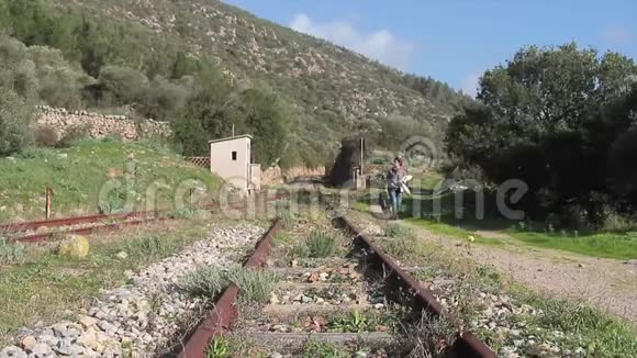 一个女人走在一条旧的废弃铁路的铁轨旁提着手提箱视频的预览图