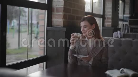 有魅力的女孩喜欢在咖啡休息时喝卡布奇诺坐在一张靠窗户的桌子旁坐在昂贵的桌子旁视频的预览图