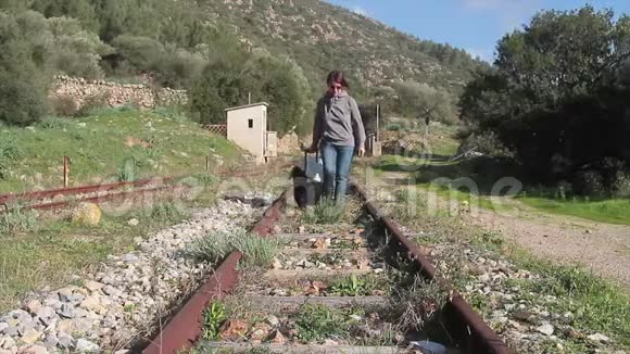 一个女人带着她的手提箱走在一条废弃铁路的铁轨中间视频的预览图