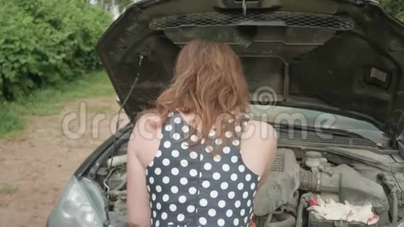 后面的女孩穿着有斑点的衣服靠近汽车带着打开的引擎盖女孩笑着满意地转过身来擦着额头视频的预览图