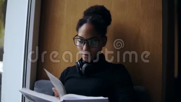 这位年轻有魅力的美国黑人妇女正在大窗台上看书时尚的特写肖像视频的预览图