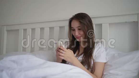 女人早上躺在床上用手机看信息视频的预览图