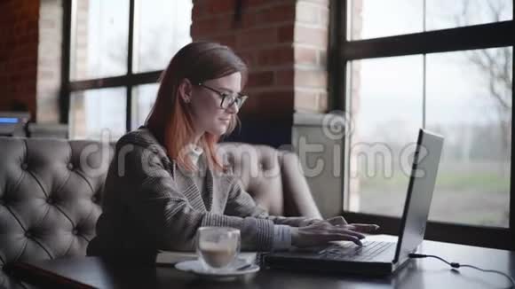 成功女性戴眼镜在笔记本电脑上工作在网上学习咖啡时写笔记本的肖像视频的预览图