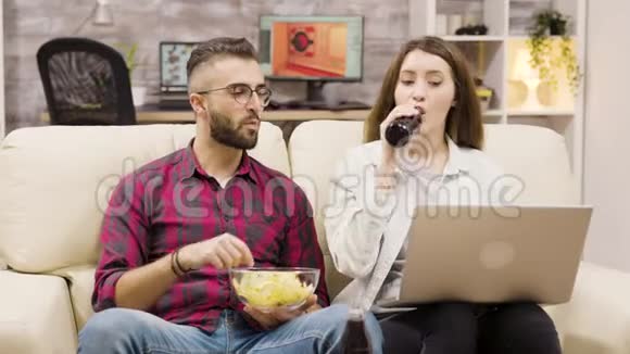 两个人一边喝汽水一边吃薯片一边浏览笔记本电脑视频的预览图