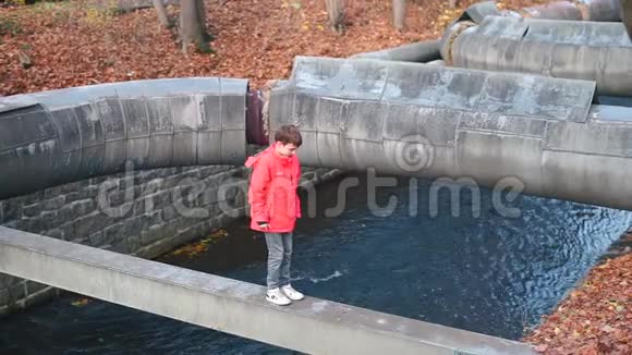 一个少年沿着城市里一条河流上方的一条细梁行走视频的预览图