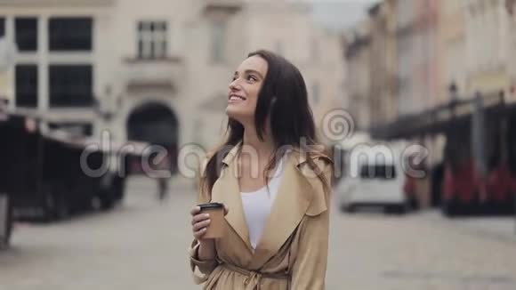 游客美丽的年轻快乐的女孩拿着纸咖啡杯微笑着走着放松地看着老城区视频的预览图