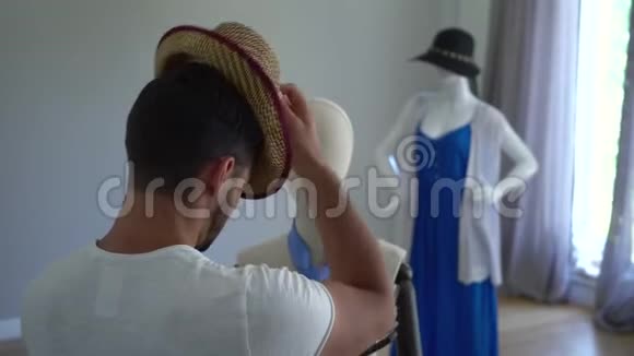 从后面看年轻人把帽子戴在头上看着男模特他在缝纫方面很开心视频的预览图