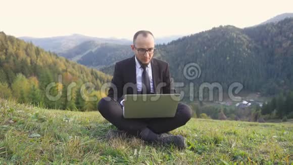 一个成年人坐在山上的时候有一个笔记本电脑放在膝上视频的预览图