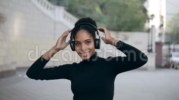 快乐的非洲女人戴着无线耳机在空荡荡的街道上听音乐下班后放松有趣视频的预览图