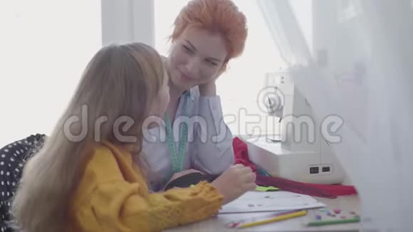 可爱的小女儿学习如何缝纫红头发的母亲向女孩展示如何选择衣服的纽扣视频的预览图