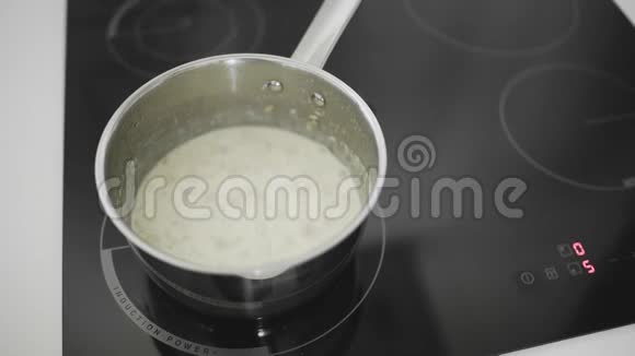 厨房灶台上的金属平底锅内有煮牛奶的燕麦片视频的预览图