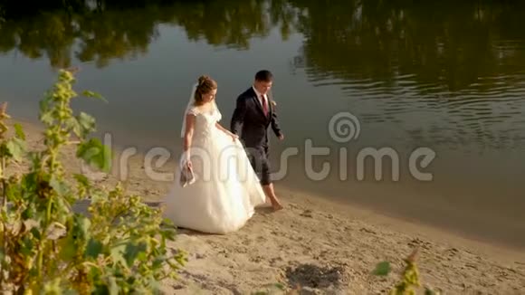 年轻的家庭在蜜月旅行亲爱的夫妇在海滩上手拉手白衣新娘视频的预览图