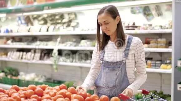 穿牛仔布的年轻女性正在杂货店挑选新鲜西红柿视频的预览图