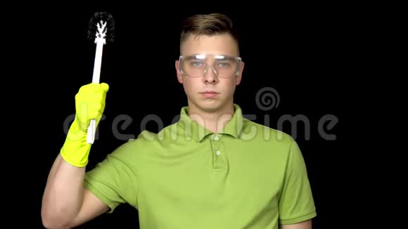 一个年轻人手里拿着马桶刷露出肱二头肌戴安全眼镜和手套清洁厕所的人视频的预览图