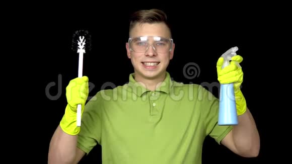 一个年轻的清洁工拿着清洁工具微笑着人戴安全眼镜和手套清洁厕所那个家伙视频的预览图