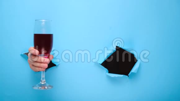 接近的女性手里拿着一杯红酒并显示了一个好的标志撕裂的蓝色纸墙视频的预览图