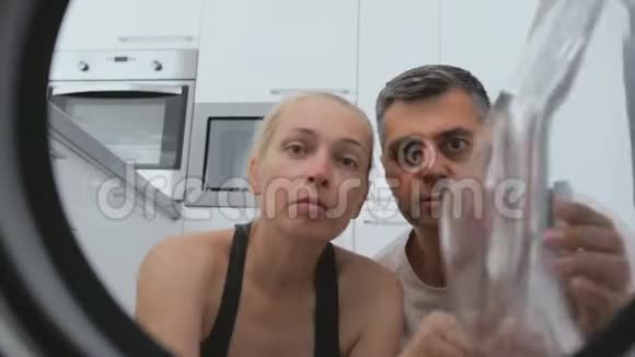 一个女人和一个男人坐在洗衣机前面惊讶地看着里面的鼓拍摄是从视频的预览图