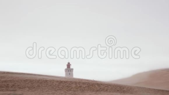 在沙尘暴中缓慢运动的大沙丘后面的远离RubjergKnude海滩灯塔的大气背景视图视频的预览图