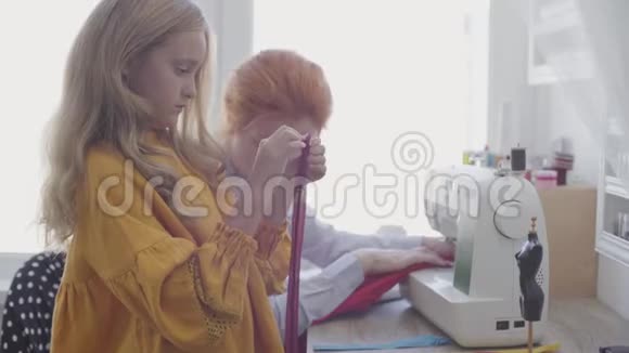 小女儿在前景中玩拉链而她的红头发的母亲则坐在桌子旁边缝衣服视频的预览图
