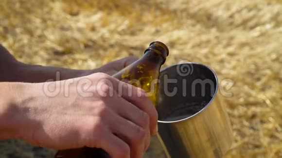 一个人把啤酒倒进麦田里的金属玻璃里上面有捆新鲜啤酒太阳场视频的预览图