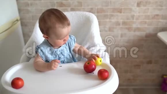婴儿吃苹果可爱的小女孩在高椅子上吃和玩苹果可爱的孩子品尝水果健康饮食c视频的预览图