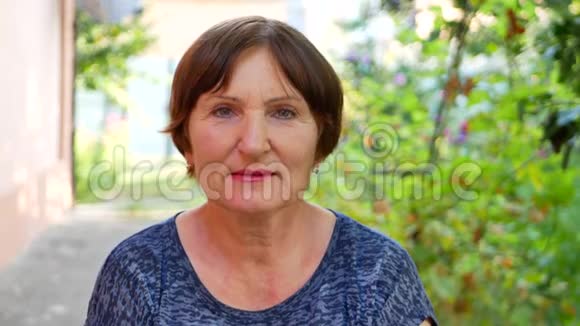 绿色植物背景下的老女人微笑视频的预览图