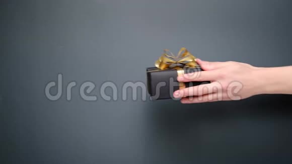 女手赠送手工黑色礼盒灰色背景上有金色丝带情人节视频的预览图