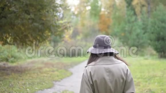 一个戴着帽子和斗篷的女人慢慢地穿过秋天的公园视频的预览图