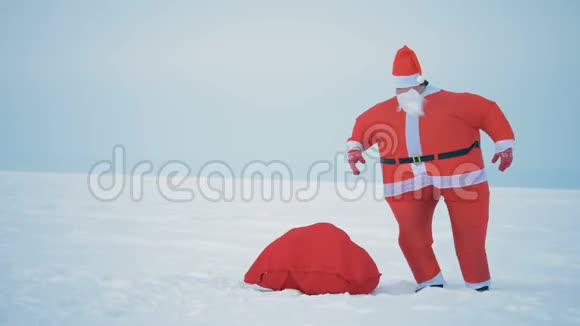 穿着圣诞老人服装的人从地上捡起一个装有礼物的袋子特写视频的预览图