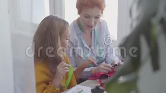 可爱的小女儿检查缝纫配件学习如何缝纫而她的红头发的母亲缝制衣服视频的预览图