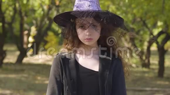 穿着万圣节女巫服装的红发白种人女孩站在秋天的公园里儿童保育视频的预览图