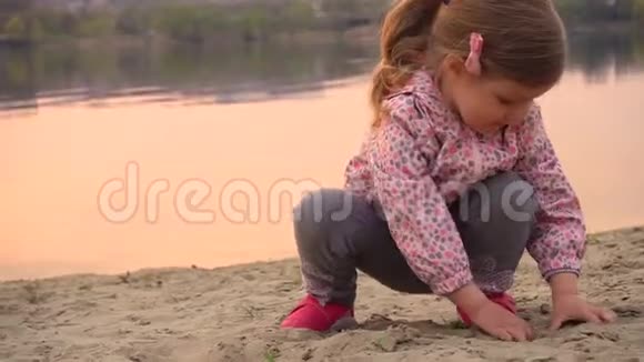 小女孩在河边或湖边的沙滩上玩沙子视频的预览图