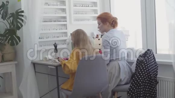 小女孩坐在前台的桌子旁红头发的妈妈在旁边缝衣服视频的预览图