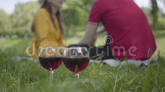两杯红酒站在草地上背景是女孩和男孩相爱在公园里约会和野餐视频的预览图