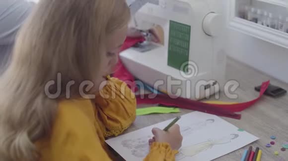 小女孩的特写镜头她坐在前台的桌子旁母亲在缝衣服视频的预览图