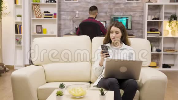 坐在沙发上用手机和笔记本电脑的女孩视频的预览图