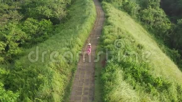 后景女子穿着红色连衣裙和草帽走在坎布汉岭的艺术家之路上在巴厘岛乌布德鸟瞰图视频的预览图