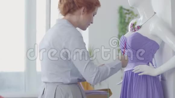 漂亮的红发女人她的女儿在房间里帮着一个模特儿穿着一件优雅的紫色连衣裙视频的预览图