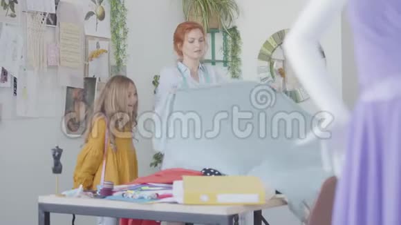 小女孩在家学习如何缝纫红发妈妈和她的女儿欣赏一块漂亮的布料视频的预览图