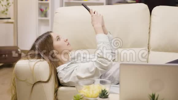 漂亮的女孩用智能手机在沙发上放松视频的预览图